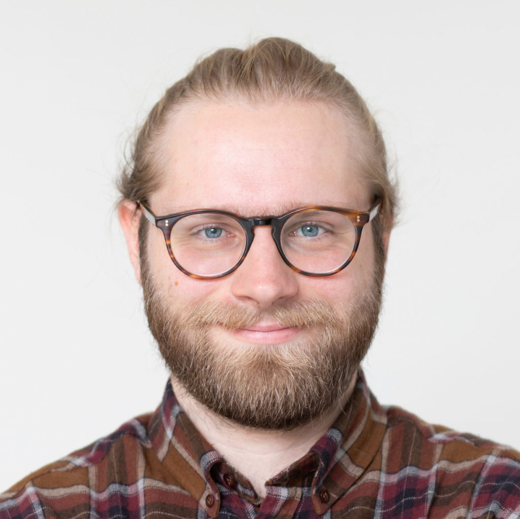 Photograph of Niels Giesselmann, a blond young man wearing glasses, a beard and a squared shirt