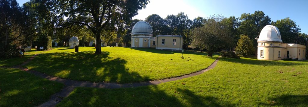 A panoramic view on the sunny park in Bergedorf in which the Hamburg Obersvatory is located: Trees and grass can be seen, also some footpaths and a couple of white and yellow old observatory domes.
