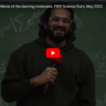 screenshot of the YouTube video preview of Nidin Vadasserys Slam at the 1st PIER science slam showing a smiling young man with a microphone in front of a blackboard with nonsensical formulas