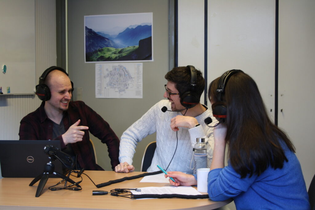 Two men and one woman sitting at a table wearing headphones, engaged in lively conversation