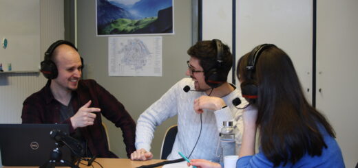 Two men and one woman sitting at a table wearing headphones, engaged in lively conversation